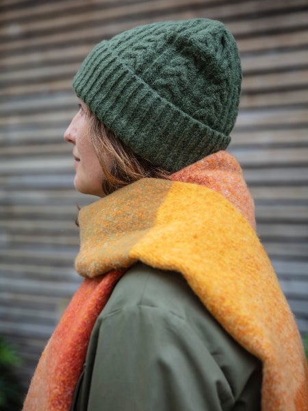 A woman wearing a khaki woollen beanie hat and orange woollen scarf