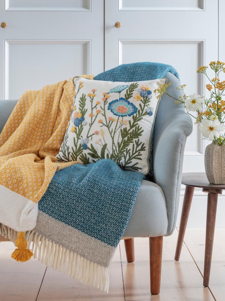 A selection of National Trust homeware, including a floral cushion with blue embroidery and throws