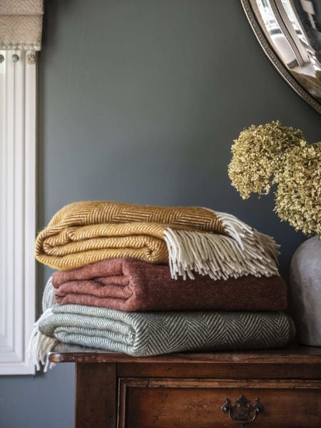National Trust wool blankets and throws in olive green burnt orange and mustard on a sideboard