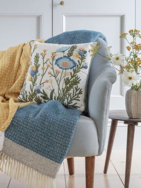 A selection of National Trust homeware, including throws, a blue cushion and ceramic jug containing flowers.