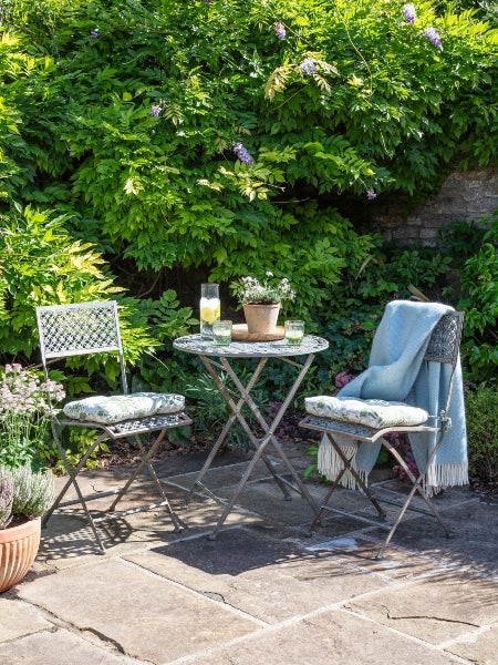 a National Trust bistro garden furniture set, styled with National Trust seat pads, a blue throw and drinking glasses on the table