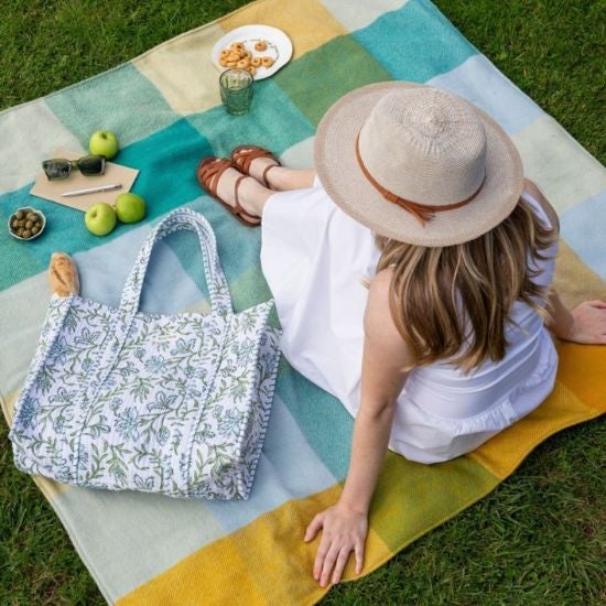 A collection of National Trust green check picnic blanket with picnic accessories laid out on the grass
