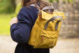 Bags - Woman wearing a National Trust crossbody bag with a colourful floral print, standing in a bright, leafy setting.