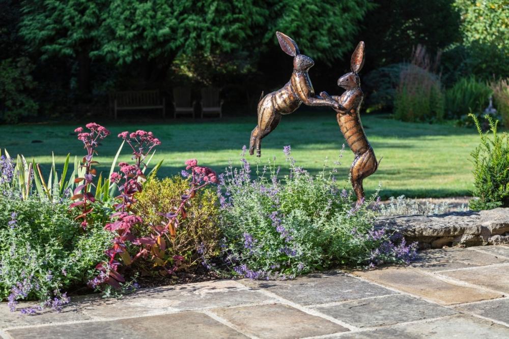 National Trust boxing hares sculpture amongst a flowering garden border.