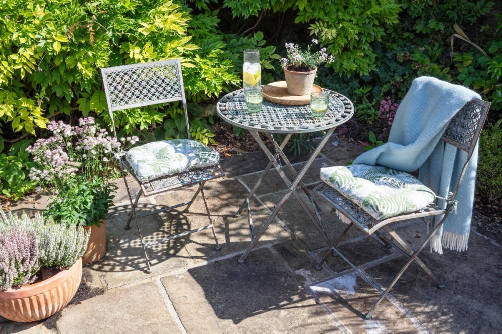 National Trust outdoor garden furniture with a green fern pattern seat pad and duck egg blue throw.