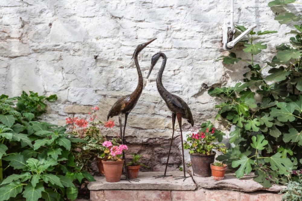 National Trust recycled metal heron sculpture displayed in a garden boarder with orange flowers.