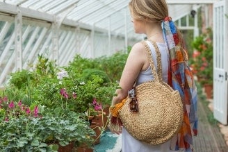 Bags - Woman wearing a National Trust crossbody bag with a colourful floral print, standing in a bright, leafy setting.
