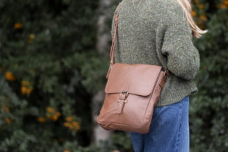 Bags - Woman wearing a National Trust crossbody bag with a colourful floral print, standing in a bright, leafy setting.