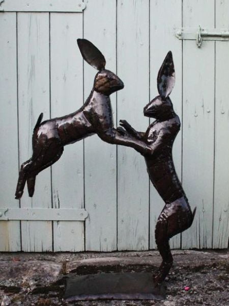 National Trust recycled metal boxing hares sculpture in a garden boarder.