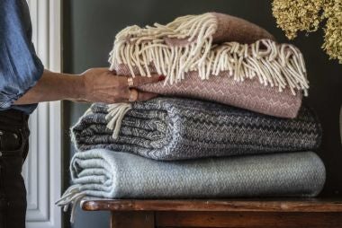 Image shows a Tweedmill Petrol blue national trust throw on a wooden bench