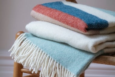 Image shows a Tweedmill Petrol blue national trust throw on a wooden bench
