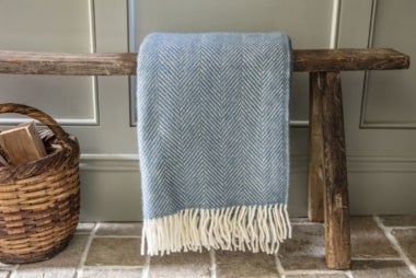 Image shows a Tweedmill Petrol blue national trust throw on a wooden bench