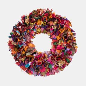 Multicoloured recycled fabric wreath featuring densely layered strips of upcycled textiles in vibrant pink, purple, orange, red, blue and green tones, creating a richly textured circular design for festive home décor.