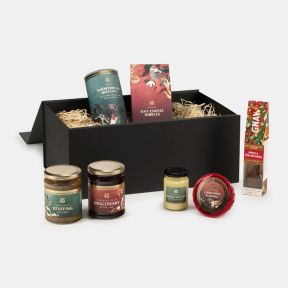 Taste of Christmas food hamper gift set presented in a black keepsake box, featuring Christmas pudding, shortbread biscuits, jingl​eberry jam, stuffing chutney, brandy butter and hot chocolate, arranged in decorative shredded paper packaging.