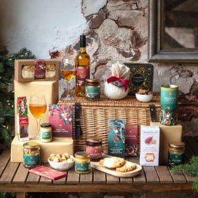Luxury Christmas hamper presented in a traditional wicker picnic basket, featuring festive food and drink gifts including ginger wine, Christmas pudding, shortbread biscuits, cranberry cookies, mince pie fudge, brandy butter, chutneys, preserves, crackers