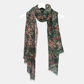 Green botanical print scarf with an all-over foliage and berry pattern, featuring soft lightweight fabric, fringed edges, and a long rectangular design draped on a hanger.