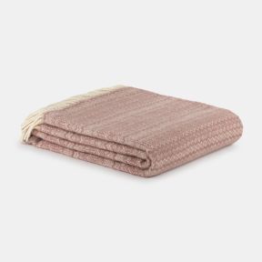 Folded blush pink throw blanket with a soft, cosy woven texture, neatly stacked on a light grey background. Finished with cream fringe tassels and a subtle herringbone-inspired pattern, it offers a warm and inviting look for sofas, beds or armchairs.