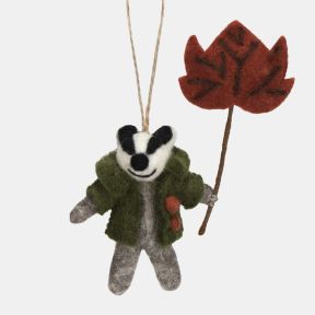 Felt badger hanging decoration wearing a green coat with orange button details and holding a large red-brown autumn leaf on a stem. Crafted with a grey felt body, black-and-white facial markings, and a natural hanging loop, making it a charming seasonal o