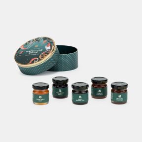 Gift box of cheese accompaniments featuring five miniature jars in a decorative round keepsake tin, including cider apple jelly, cranberry sauce, onion marmalade, tomato chutney and real ale chutney, displayed on a white background.