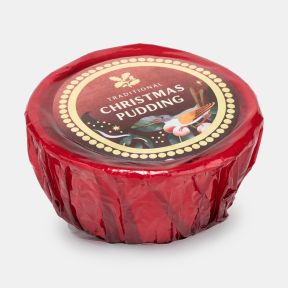 Traditional Christmas pudding wrapped in red cellophane with a festive Christmas label featuring holly leaves, berries and a bird, shown at an angled view.
