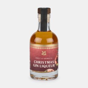 Bottle of sweet and aromatic Christmas gin liqueur with a festive illustrated label and wooden-effect stopper, presented on a light grey background.