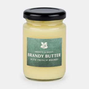 Jar of smooth and boozy brandy butter with French brandy, featuring a green label and black lid, presented on a light grey background.