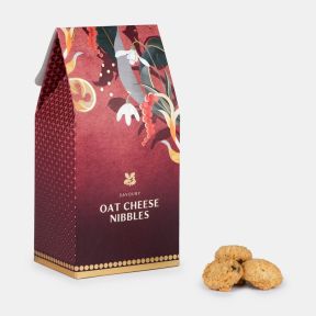 Savoury oat cheese nibbles in a festive burgundy gift box with gold accents and decorative seasonal botanical illustrations, displayed alongside three oat cheese biscuits.
