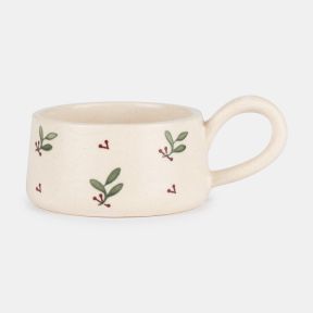 Hand-painted ceramic tealight holder with a rounded loop handle, featuring a cream glazed finish decorated with green leaves and red berry sprigs, shown in side profile to showcase the festive botanical pattern and handcrafted design.