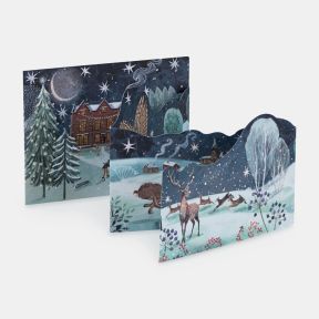 Illustrated freestanding advent calendar featuring a snowy winter countryside scene with deer, a badger, cottages and snow-covered trees beneath a star-filled night sky. The concertina-style calendar includes numbered advent doors integrated into the artw