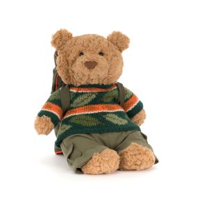 Jellycat teddy bear plush dressed for adventure, featuring soft beige fur, a green camouflage-style knitted sweater with orange and white stripes, khaki trousers, and a backpack. The bear is seated against a plain light background.