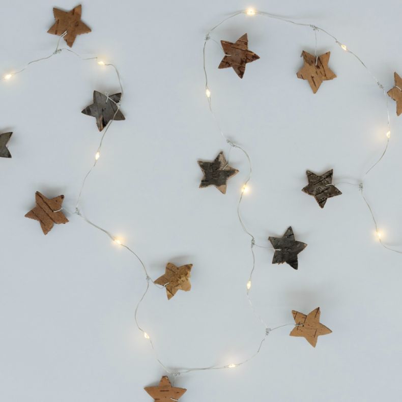 LED birch star garland arranged in gentle loops against a light background, featuring natural birch wood star ornaments suspended from a delicate silver wire string with integrated warm white LED lights. The stars display natural variations in bark textur