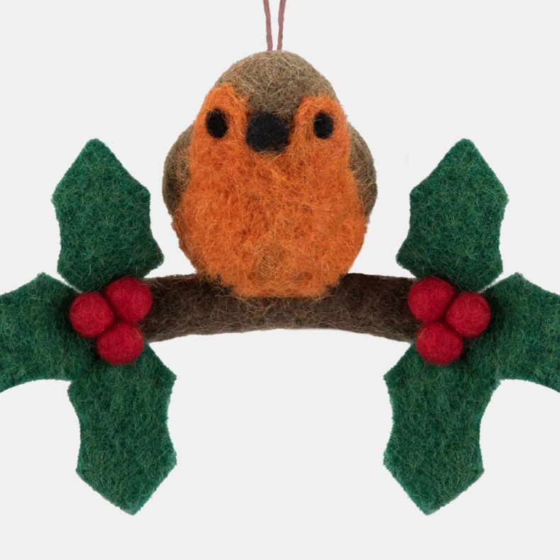 Close-up detail of a handcrafted felt robin hanging decoration, featuring a rounded robin with a bright orange breast, brown body and black felt eyes and beak perched on a curved brown branch. The branch is decorated with green felt holly leaves and clust