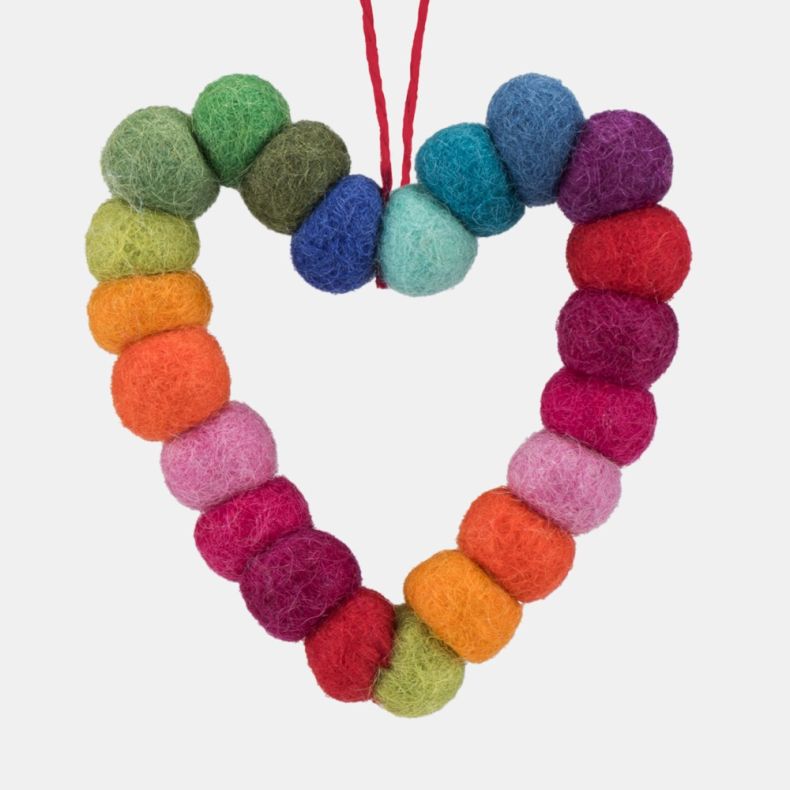 Close-up of a handcrafted heart-shaped hanging decoration made from colourful felt wool balls arranged in a rainbow gradient. The decoration features individually felted spheres in shades of green, yellow, orange, pink, red, purple and blue, threaded toge