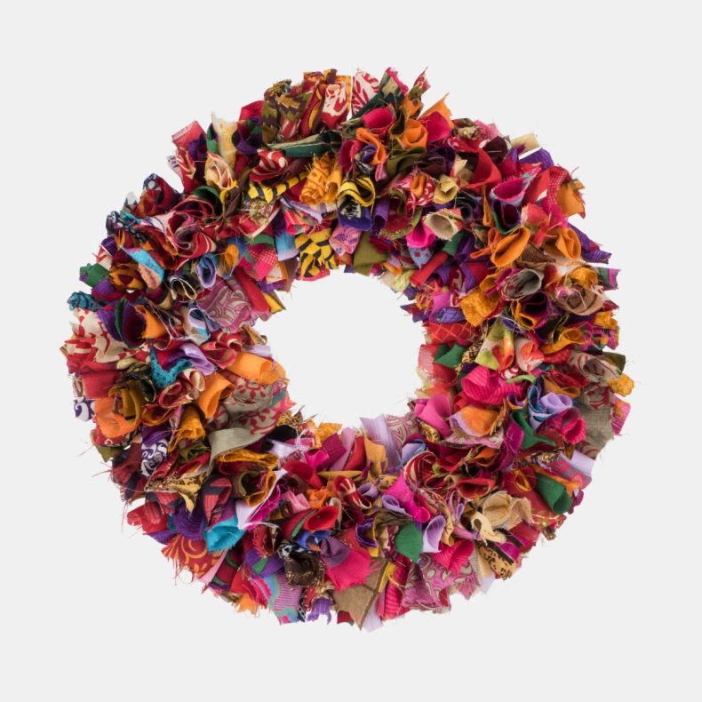 Multicoloured recycled fabric wreath featuring densely layered strips of upcycled textiles in vibrant pink, purple, orange, red, blue and green tones, creating a richly textured circular design for festive home décor.
