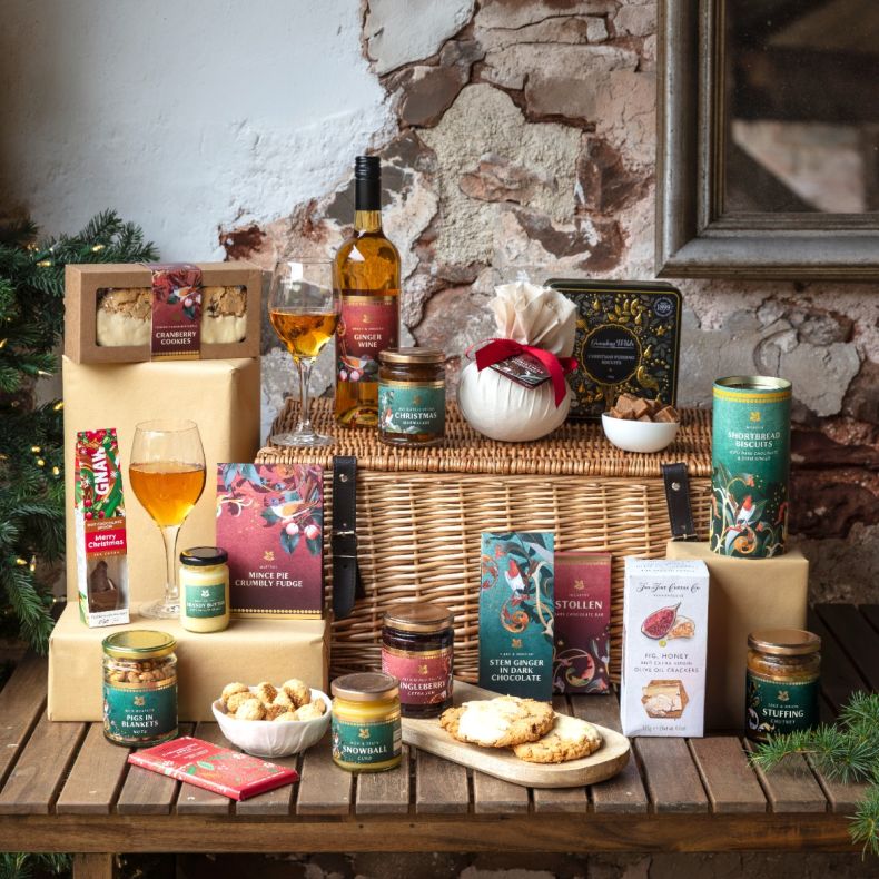 Luxury Christmas hamper presented in a traditional wicker picnic basket, featuring festive food and drink gifts including ginger wine, Christmas pudding, shortbread biscuits, cranberry cookies, mince pie fudge, brandy butter, chutneys, preserves, crackers