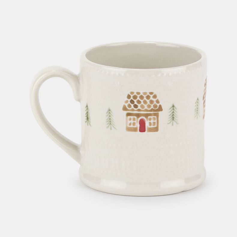 Cream ceramic mug with an embossed textured finish, featuring a festive gingerbread house and pine tree pattern in soft brown, green and red tones, shown from an angled front view with a curved handle and classic cylindrical shape.
