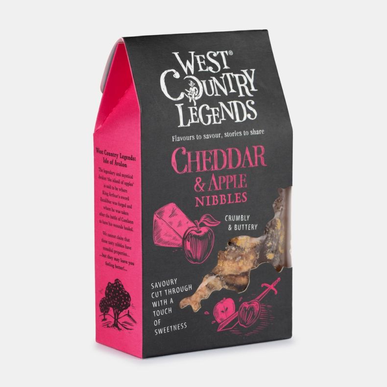 Box of West Country Legends Cheddar & Apple Nibbles, featuring black and pink packaging with illustrated cheddar cheese and apple graphics, a window showing the savoury snack pieces inside, and branding on the front and side panels, isolated on a white ba