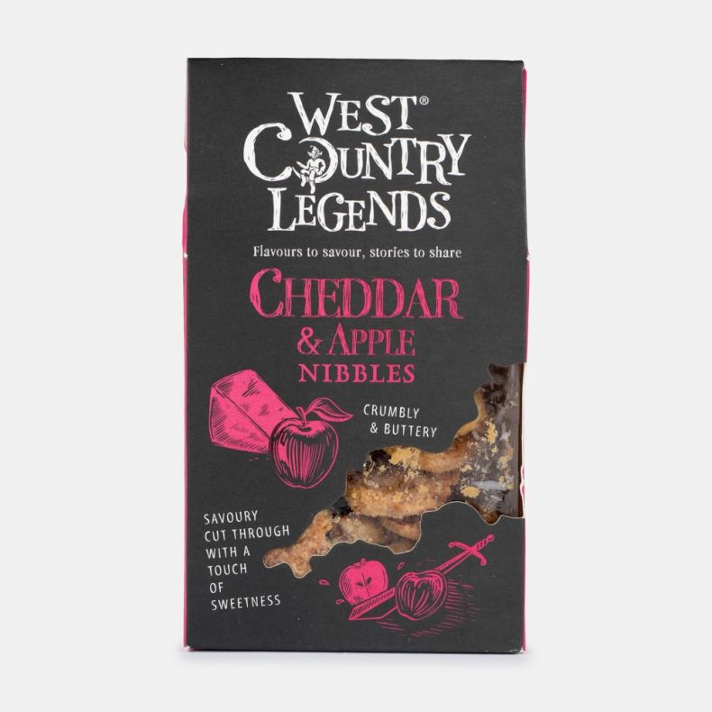 Box of West Country Legends Cheddar & Apple Nibbles, featuring black packaging with pink illustrated cheddar cheese and apple graphics, a front window displaying the savoury snack pieces inside, and product branding on the front, isolated on a white backg
