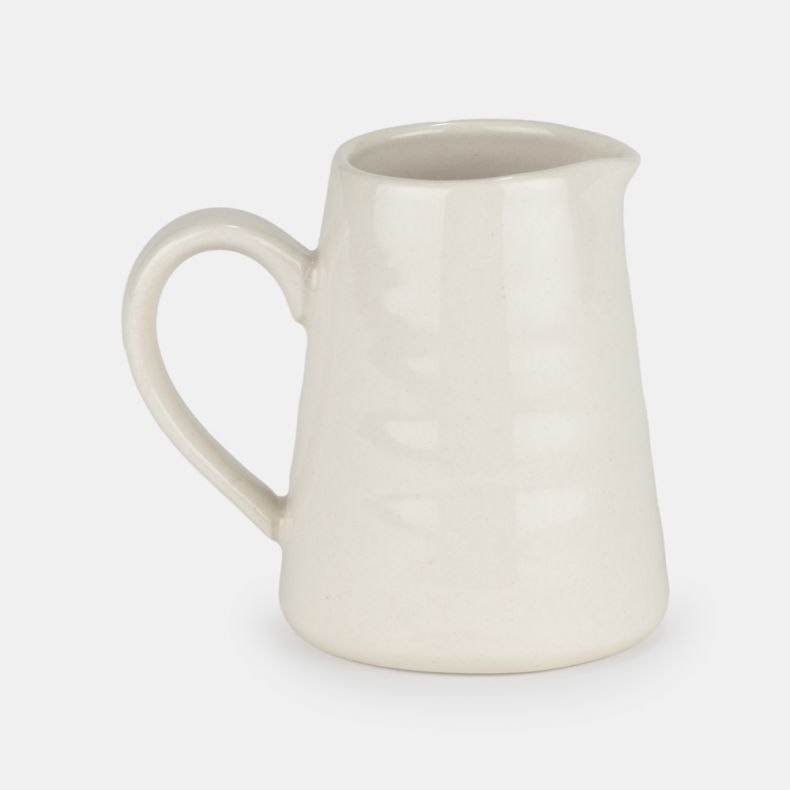 Cream ceramic milk jug shown from the reverse side, featuring a smooth glazed finish, curved handle, pouring spout, and simple tapered silhouette.