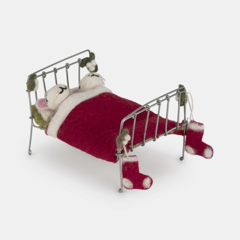 Felt mice Christmas hanging decoration in a miniature metal bed, featuring two white wool-effect mice tucked beneath a red felt blanket, with embroidered facial details, festive stocking accents, and holly-inspired decoration on the bed frame for whimsica