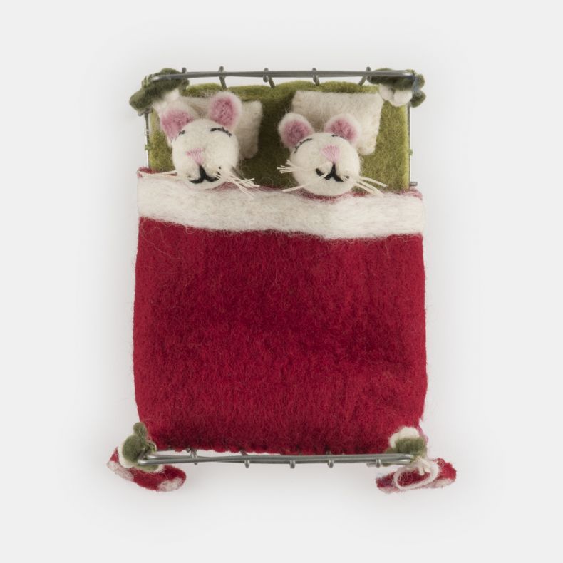 Felt mice Christmas hanging decoration in a miniature metal bed, featuring two white wool-effect mice tucked beneath a red felt blanket, with embroidered closed eyes, pink ears, whisker detailing, green felt pillows, festive stocking accents, and holly-in