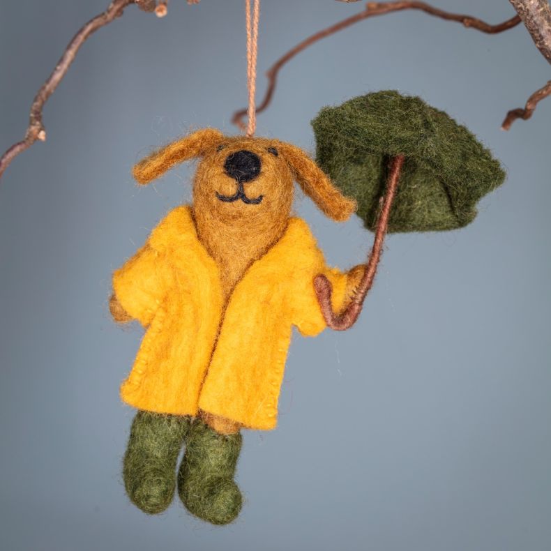 Felt hanging dog ornament wearing a yellow raincoat and green trousers, holding a green umbrella and suspended by a hanging loop decoration