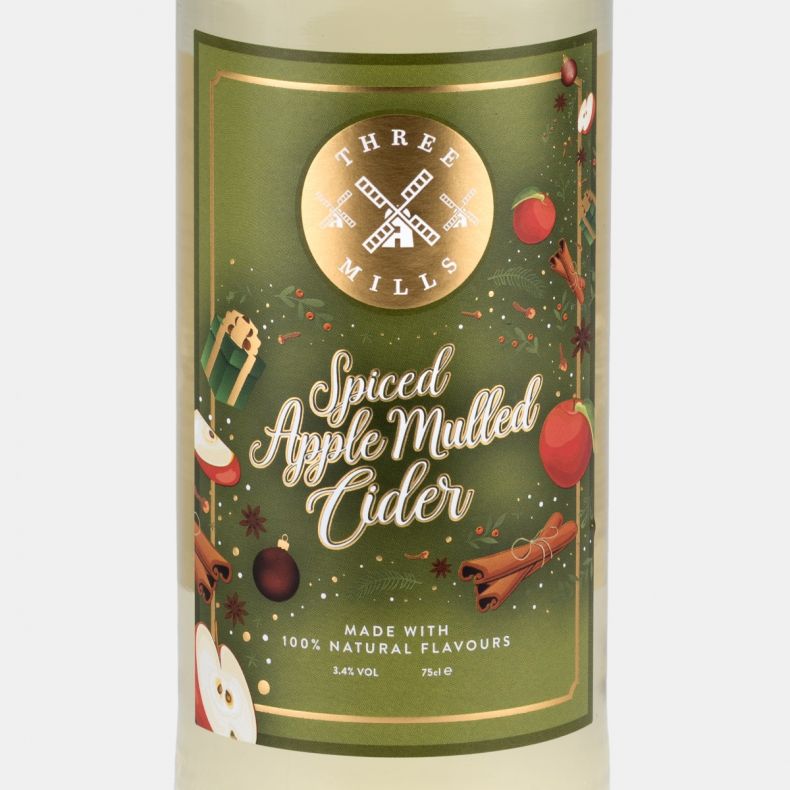 Three Mills Spiced Apple Mulled Cider label close-up, featuring a festive green design with apples, cinnamon sticks, seasonal ornaments, gift illustrations and winter foliage motifs on a 75cl cider bottle.
