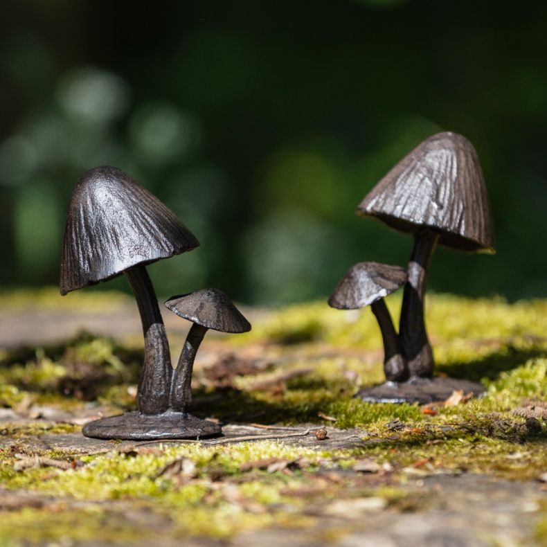 Cast iron mushroom sculptures featuring two mushrooms with textured stems and detailed caps, displayed on a moss-covered stone surface in a garden setting with a softly blurred green background.