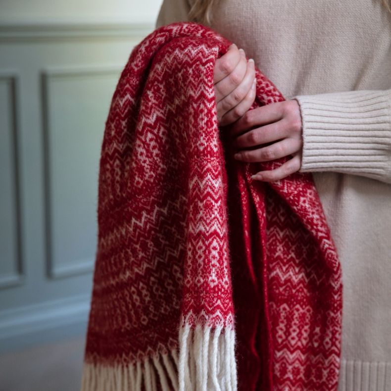 Red woven scarf with cream Fair Isle pattern and tasselled fringe, shown draped in hands to highlight the soft textured fabric and traditional winter design