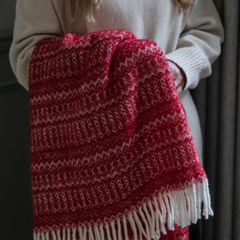 Red woven scarf with cream Fair Isle pattern and tasselled fringe, shown draped over the arm to highlight the soft textured fabric, traditional winter design and fringed edge detailing