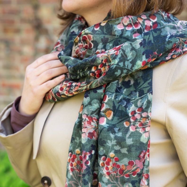 Green botanical print scarf styled around the neck with a beige coat, featuring an all-over foliage and berry pattern in shades of green, red and pink on soft lightweight fabric.