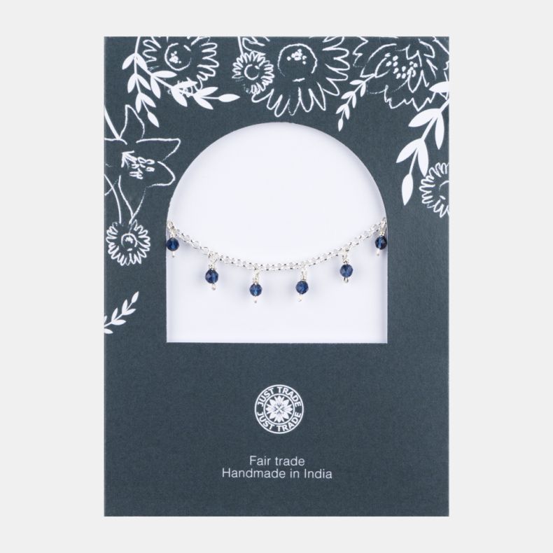 Silver-tone charm bracelet with faceted navy blue crystal bead drops, displayed on a floral Just Trade jewellery card with adjustable extender chain and lobster clasp fastening.