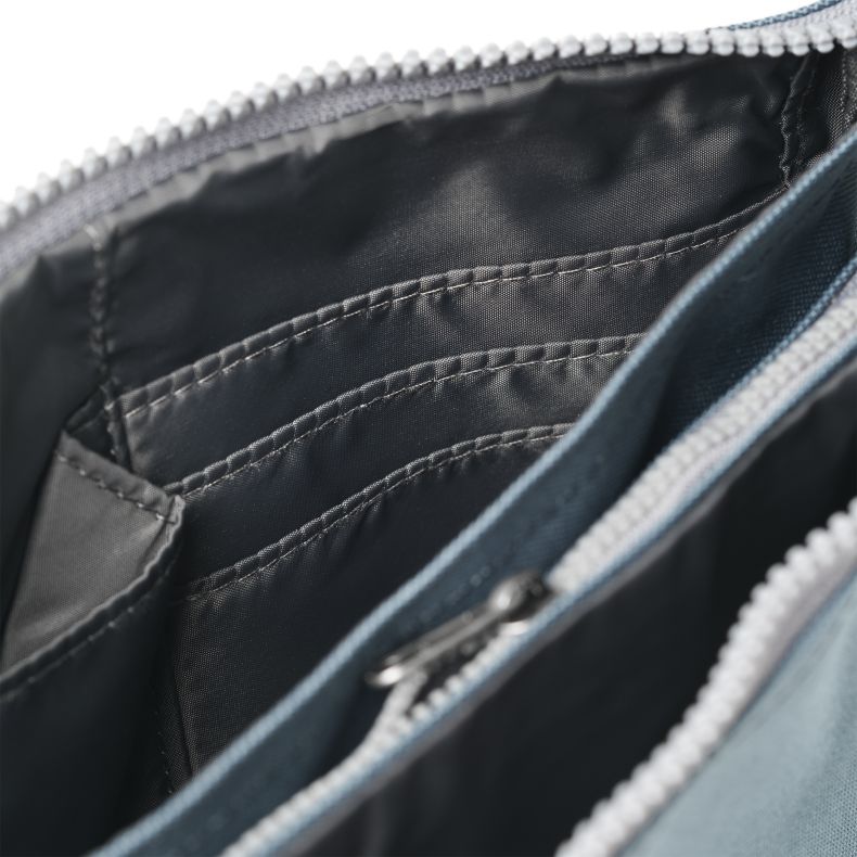 Blue-grey recycled canvas crossbody pouch interior shown in a close-up view, highlighting multiple card slots, slip pockets, durable grey lining, and organised storage compartments within the zip-top design.