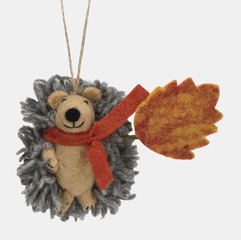 Felt hedgehog hanging decoration featuring a soft grey textured coat, beige felt face, and a bright orange scarf. Holding a large orange and yellow autumn leaf, this charming seasonal ornament is finished with a natural hanging loop and is ideal for autum